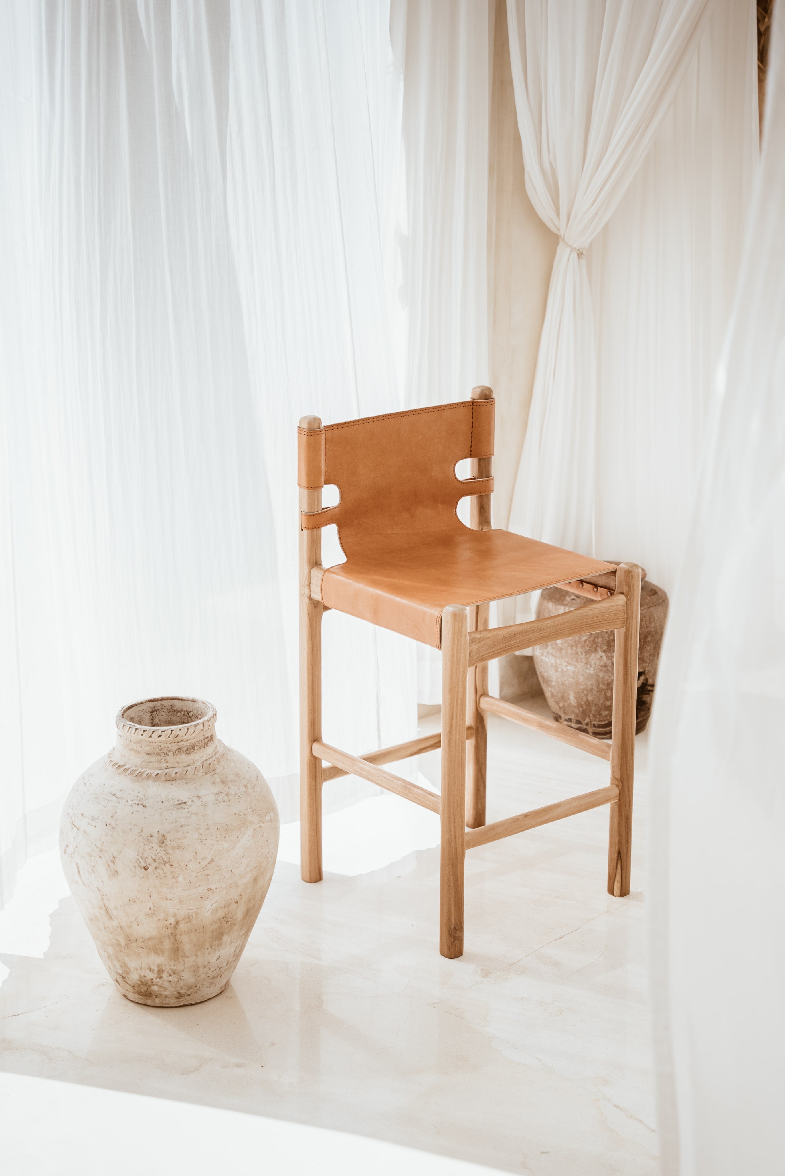 Indoor light filled room with a leather and teak stool and an organic vase