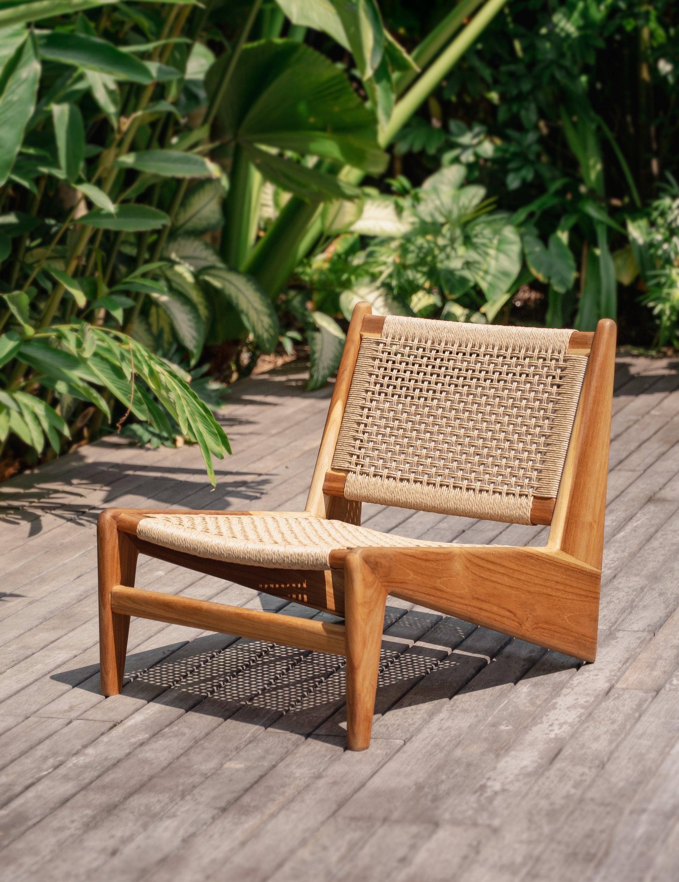 teak and rattan lounge chair on deck surrounded by lush green jungle in bali