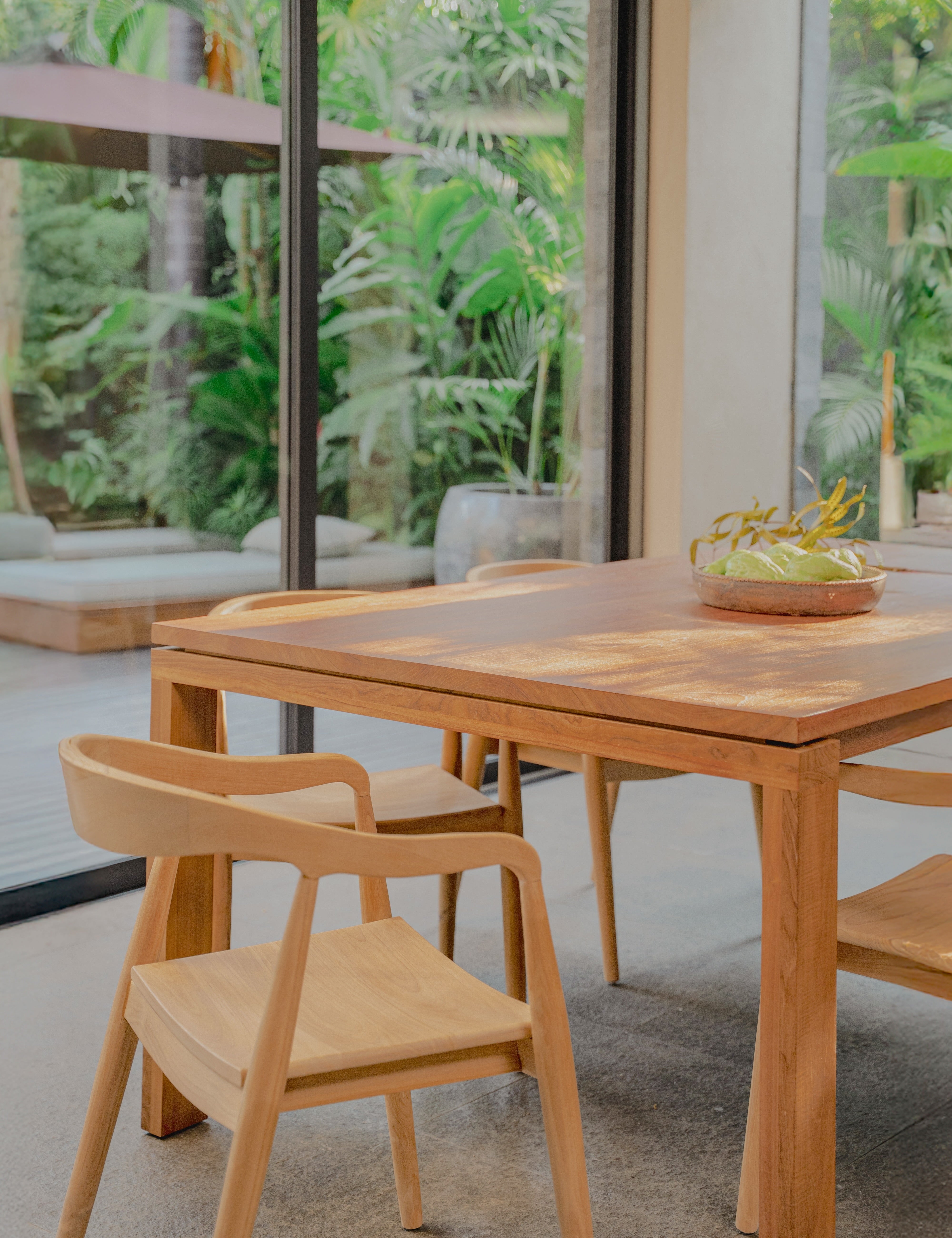 teak dining table and rounded chairs with a forest backdrop 