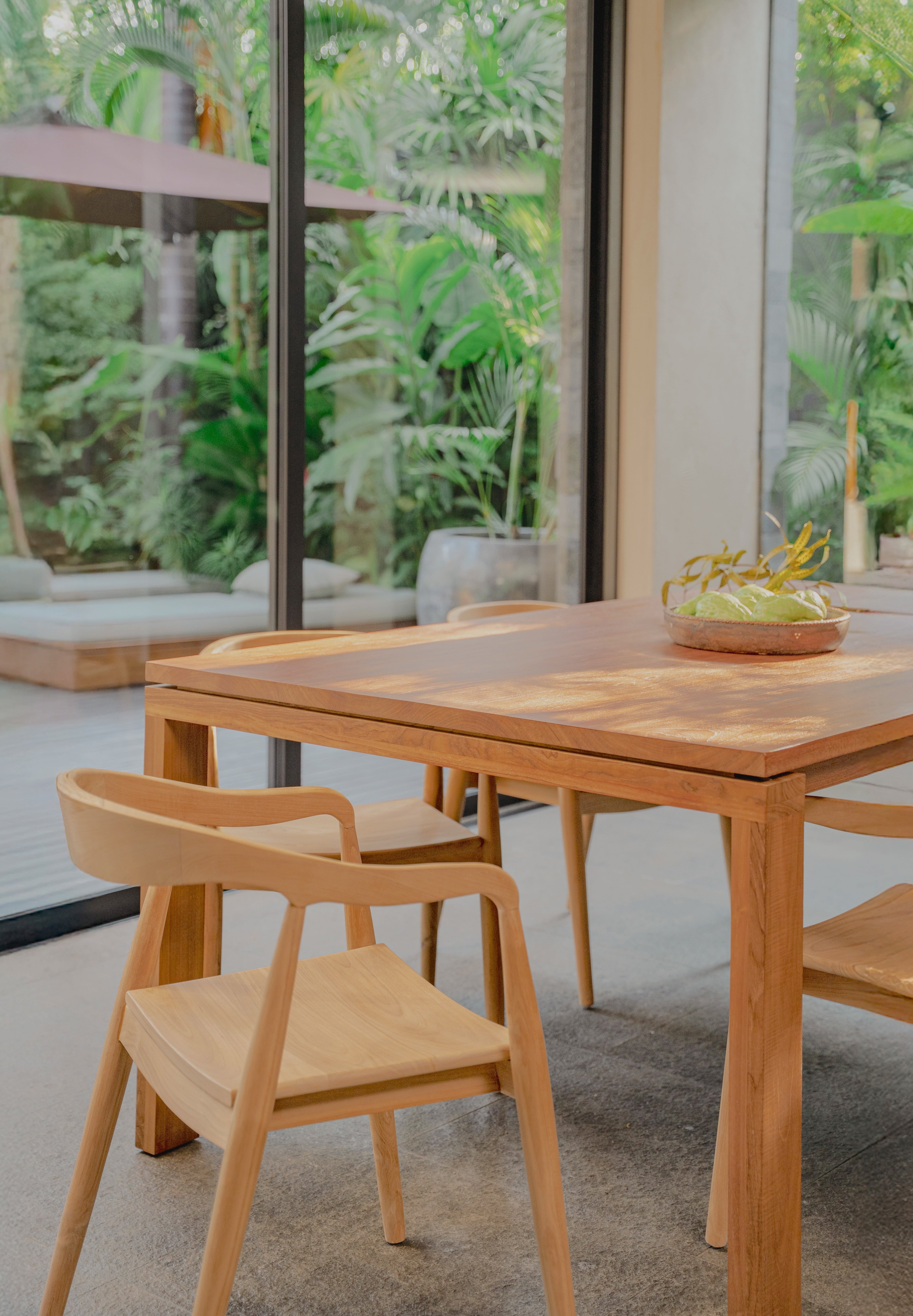 teak dining table and rounded chairs with a forest backdrop 