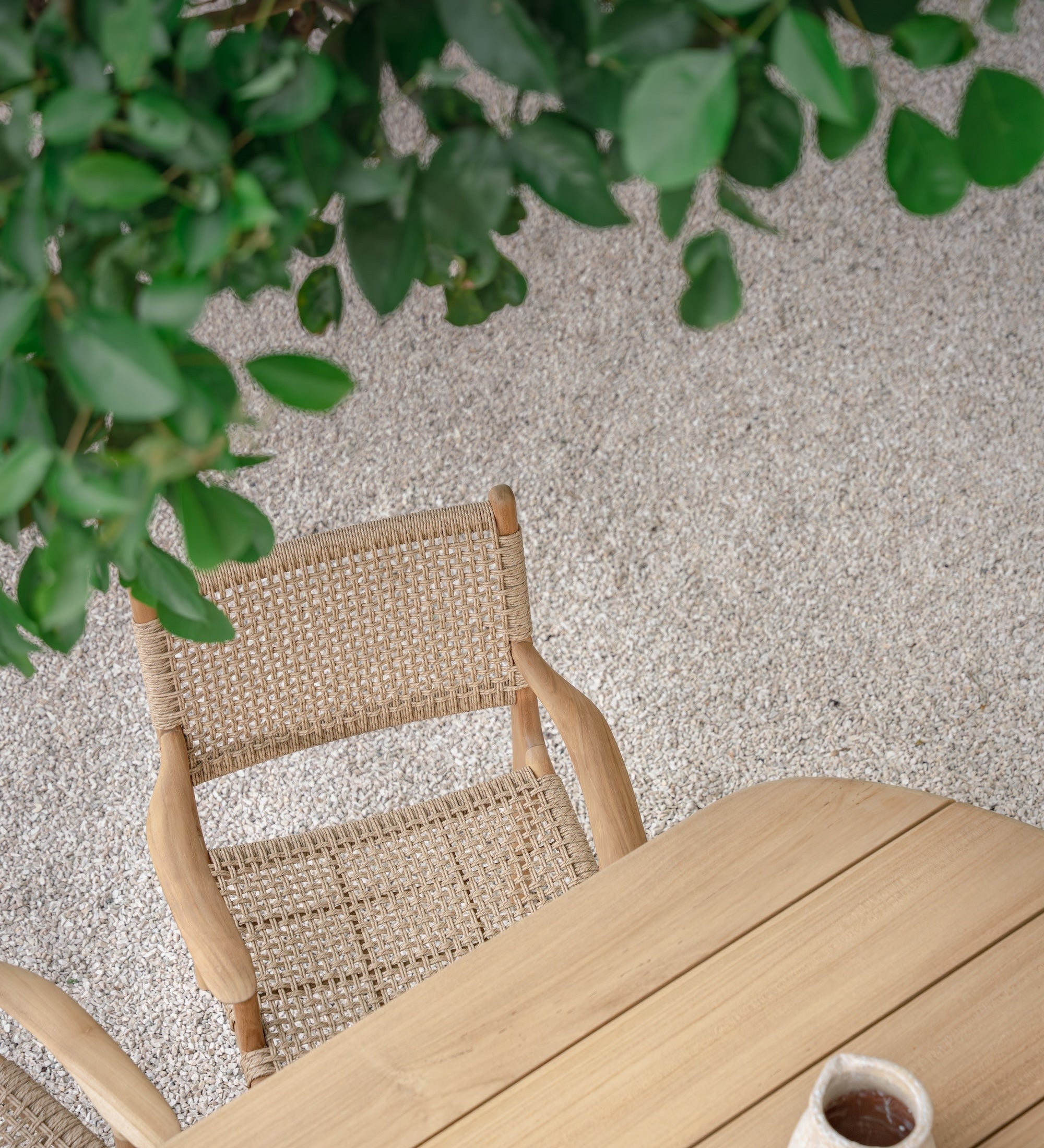 birds eye view of a rattan dining chair  and teak dining table outside with tree leaves in the top section