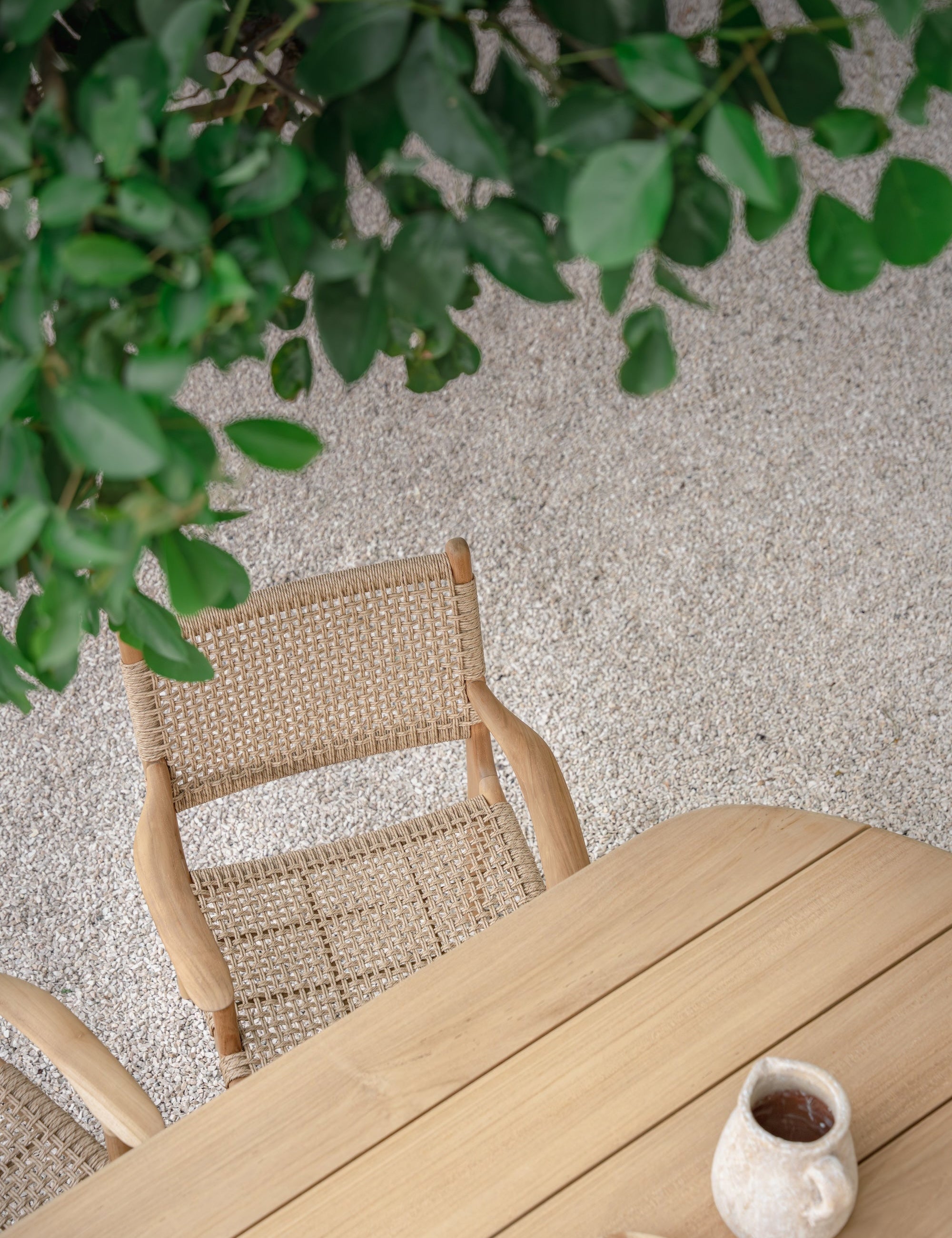 birds eye view of a rattan dining chair  and teak dining table outside with tree leaves in the top section