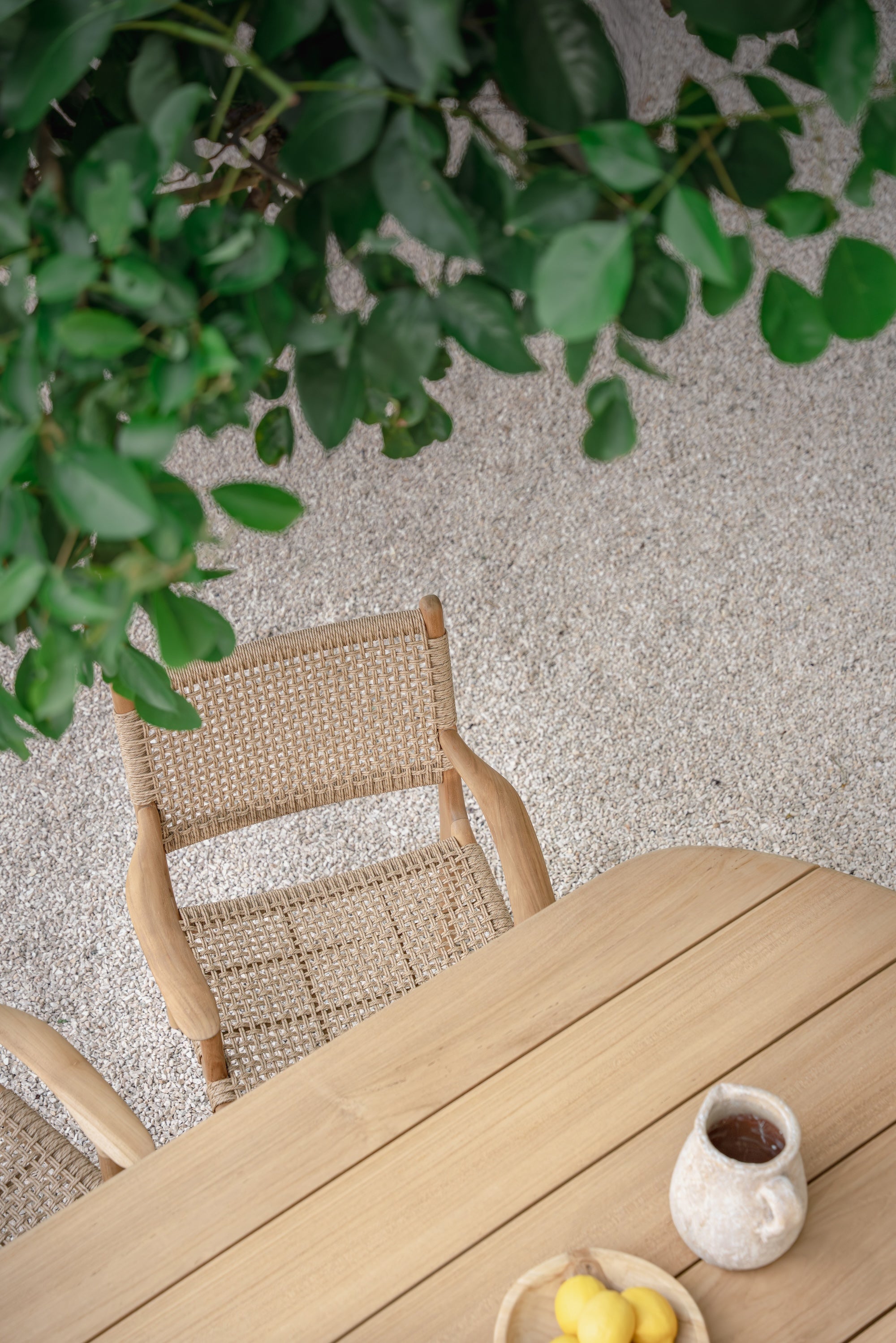 birds eye view of a rattan dining chair  and teak dining table outside with tree leaves in the top section