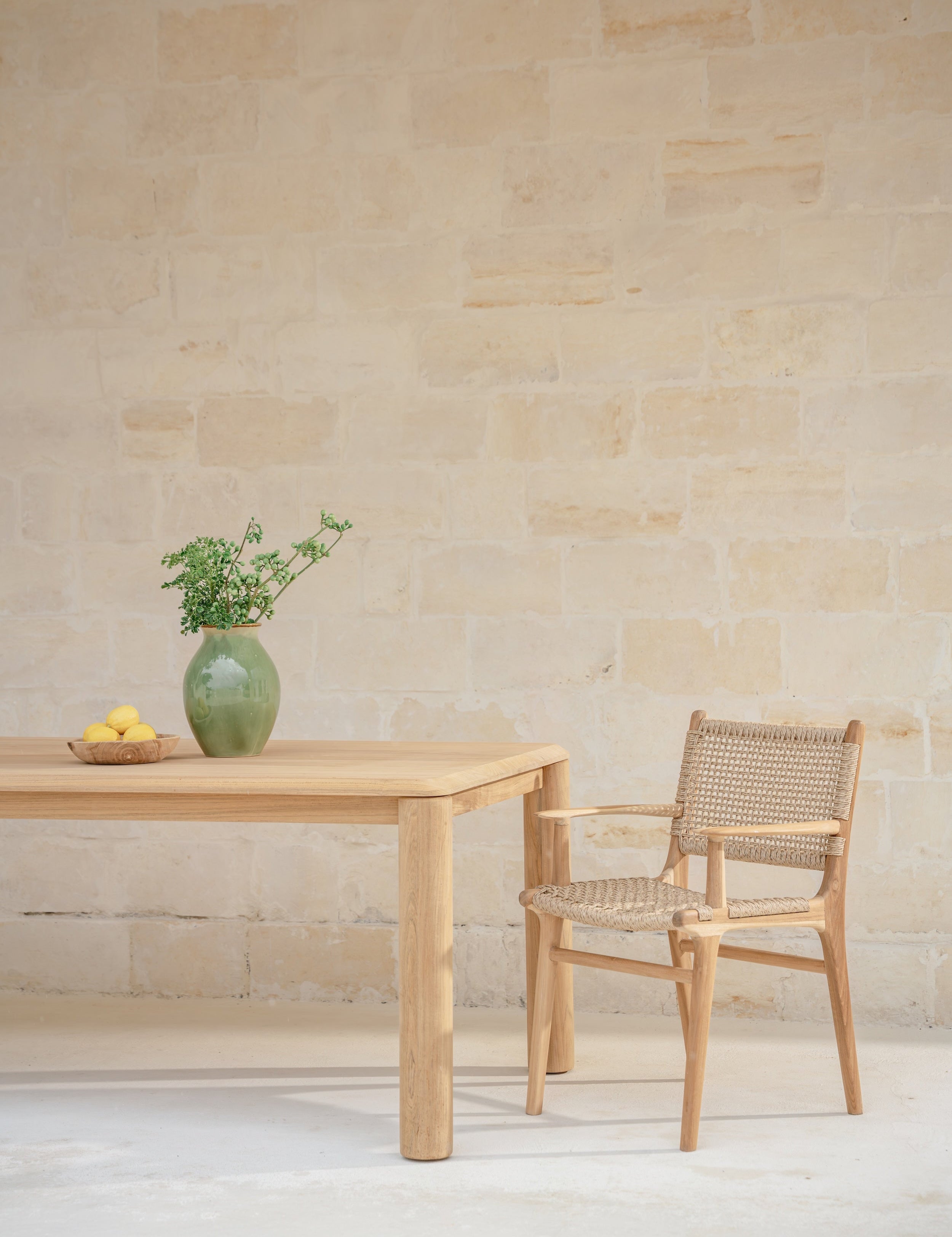 stone wall with a teak dining table and rattan and teak dining chair 