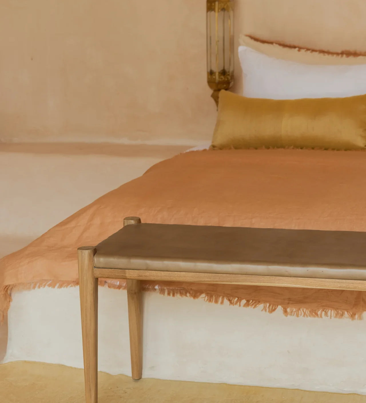 low profile white bed with golden tan bench and rust colored linen bedding