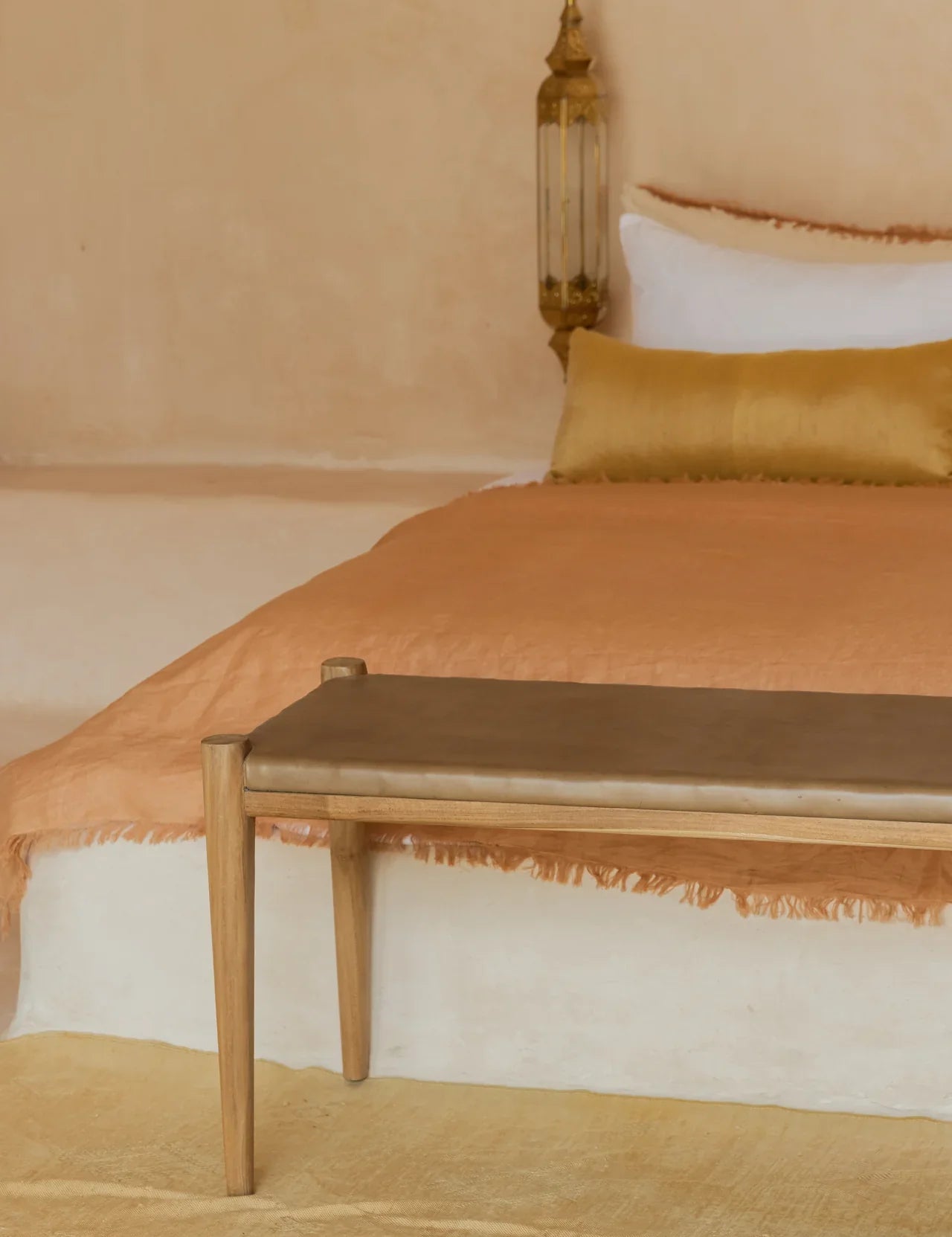low profile white bed with golden tan bench and rust colored linen bedding
