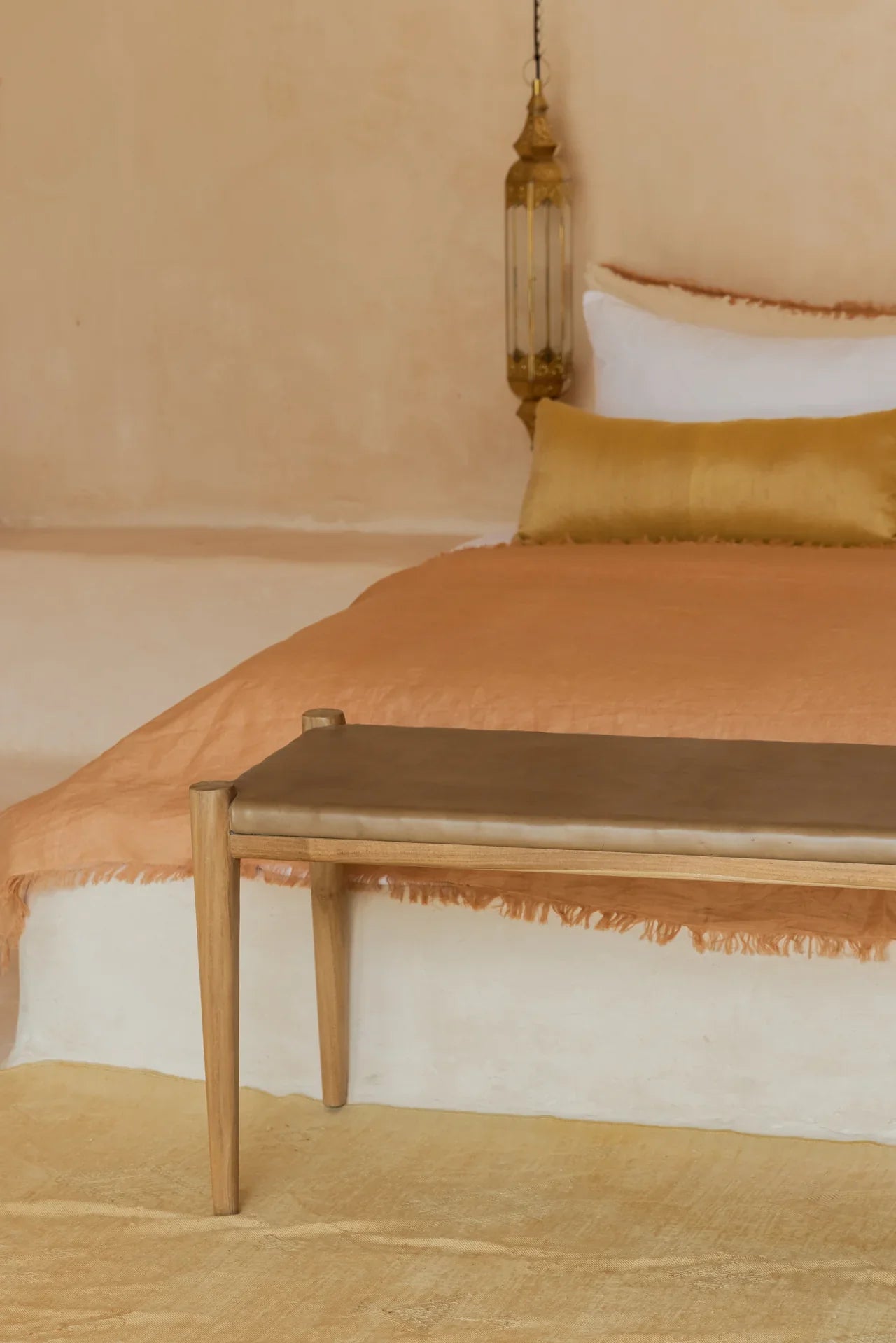 low profile white bed with golden tan bench and rust colored linen bedding