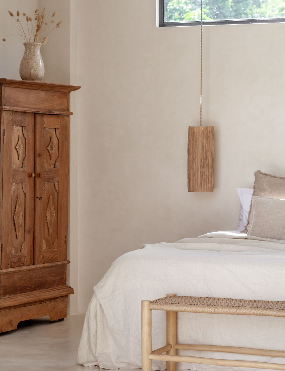 Neutral interior bedroom in bali with a teak bench at the end of the bed