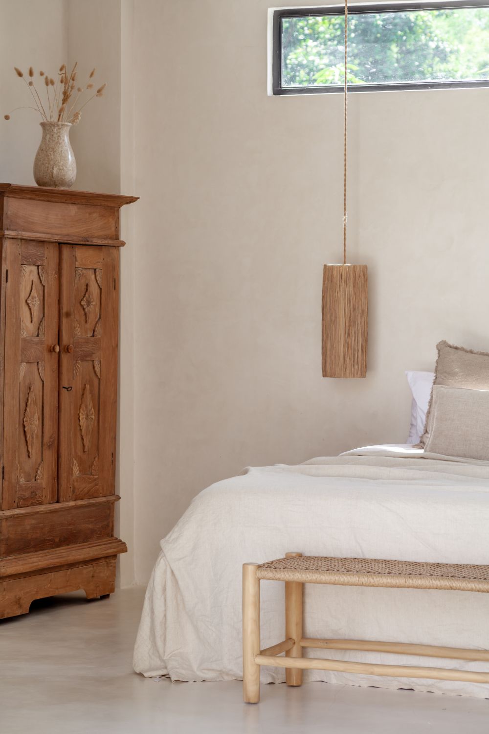 Neutral interior bedroom in bali with a teak bench at the end of the bed