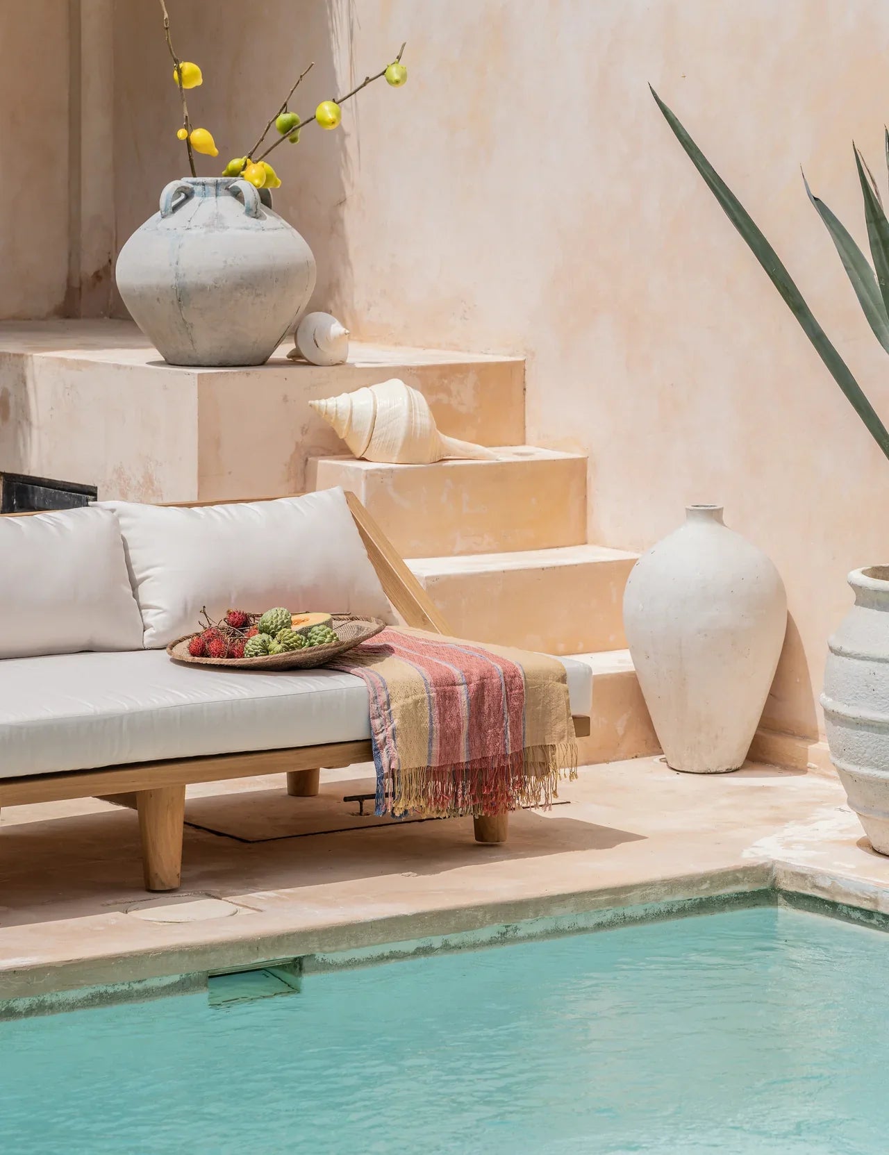 teak daybed with pillows next to a blue pool in bali