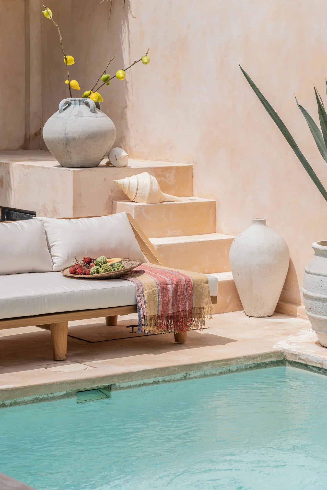 teak daybed with pillows next to a blue pool in bali