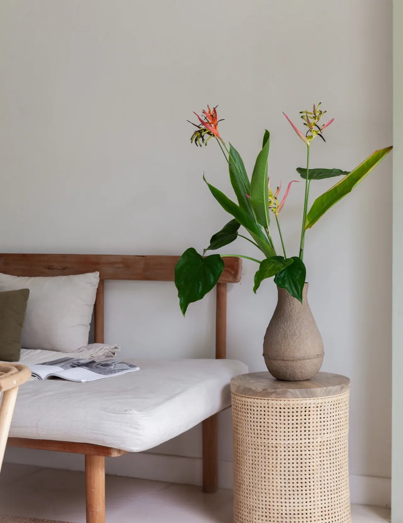 rattan side table with a plant on top next to a walnut daybed with white linen cushions.