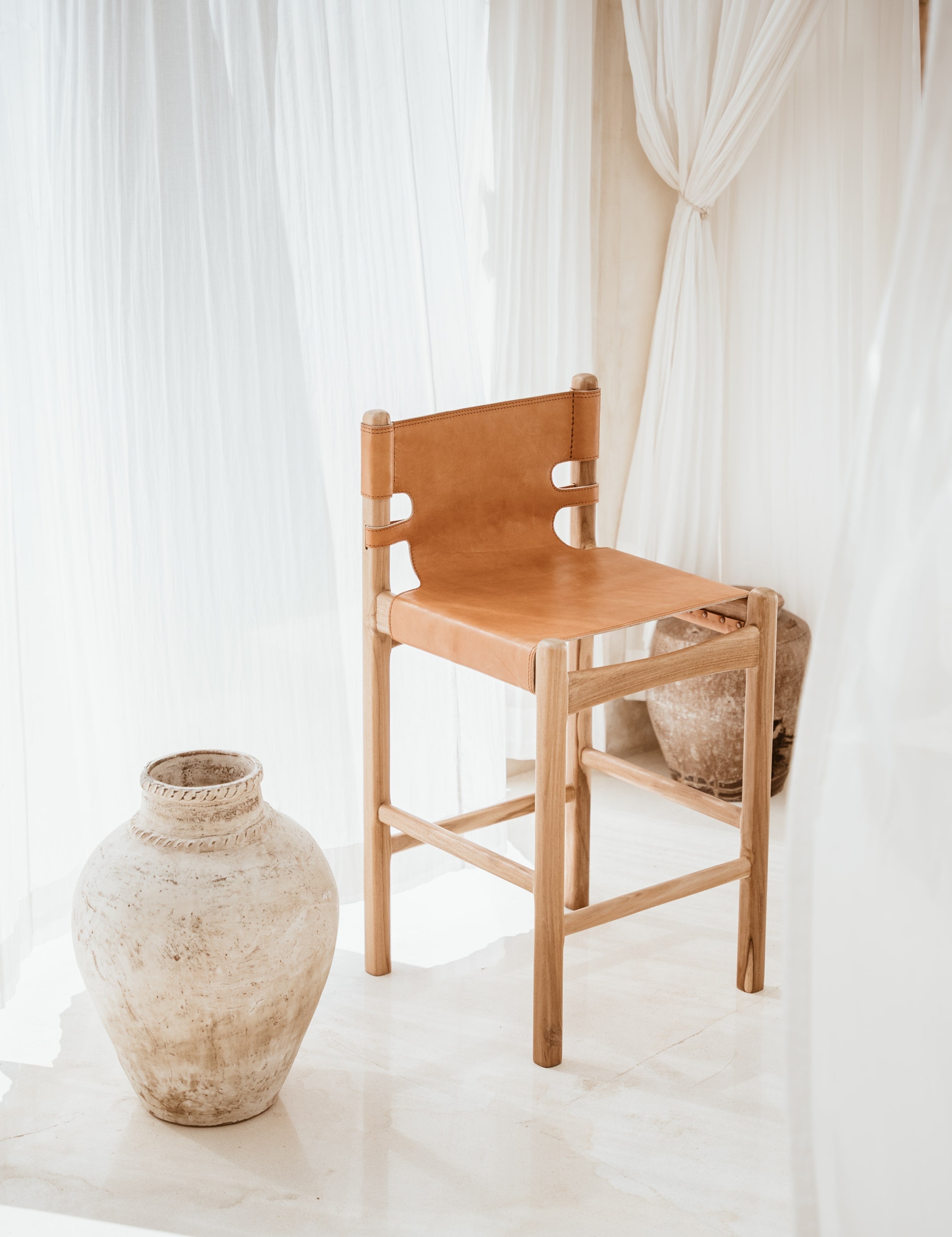 Indoor light filled room with a leather and teak stool and an organic vase