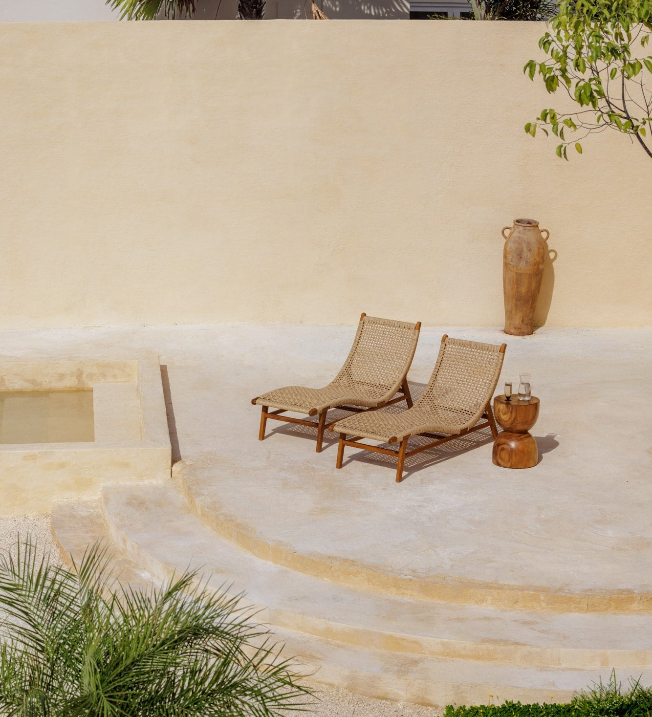 two teak and rattan lounge chairs sitting on a sun-drenched concrete deck outdoors in Bali