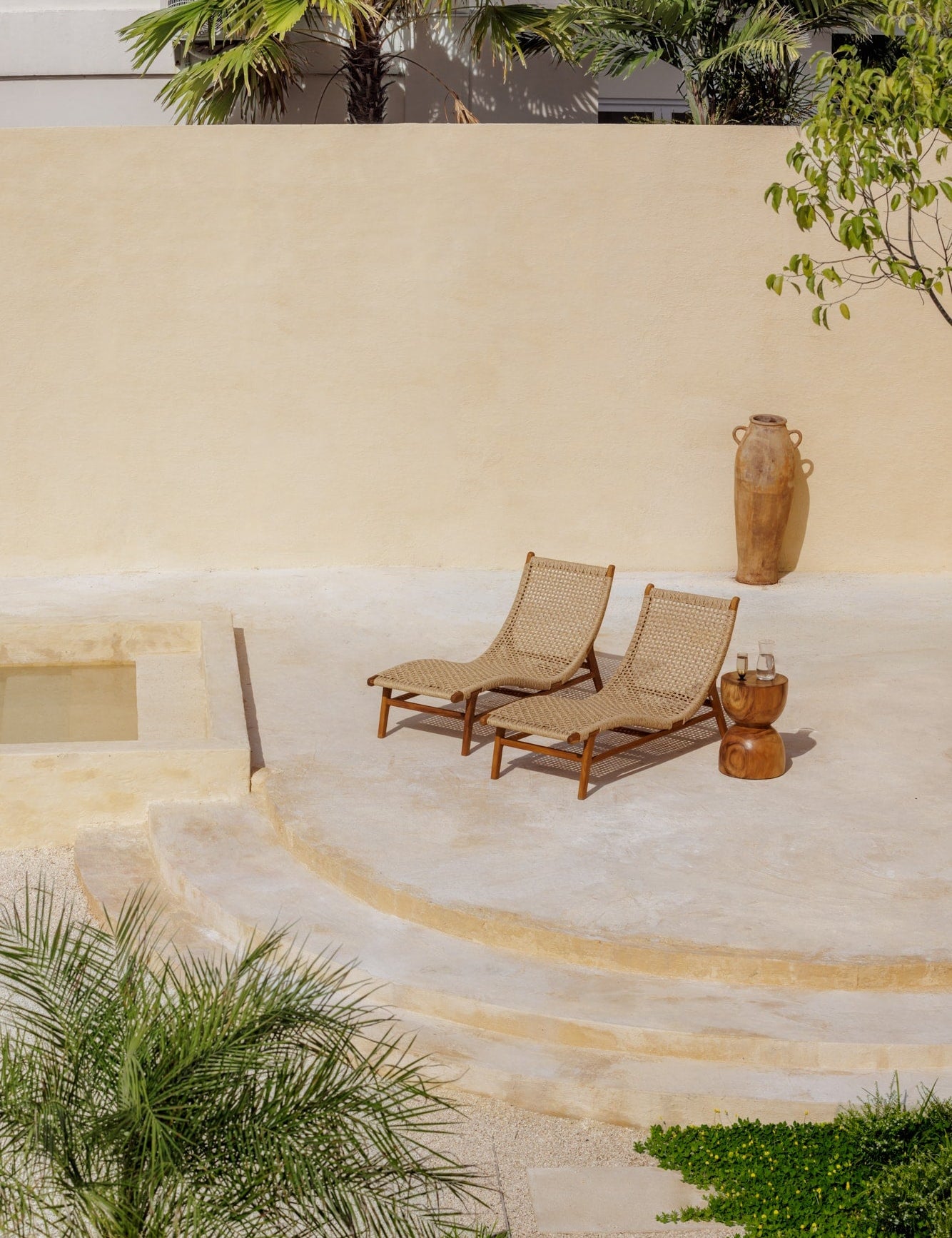 two teak and rattan lounge chairs sitting on a sun-drenched concrete deck outdoors in Bali