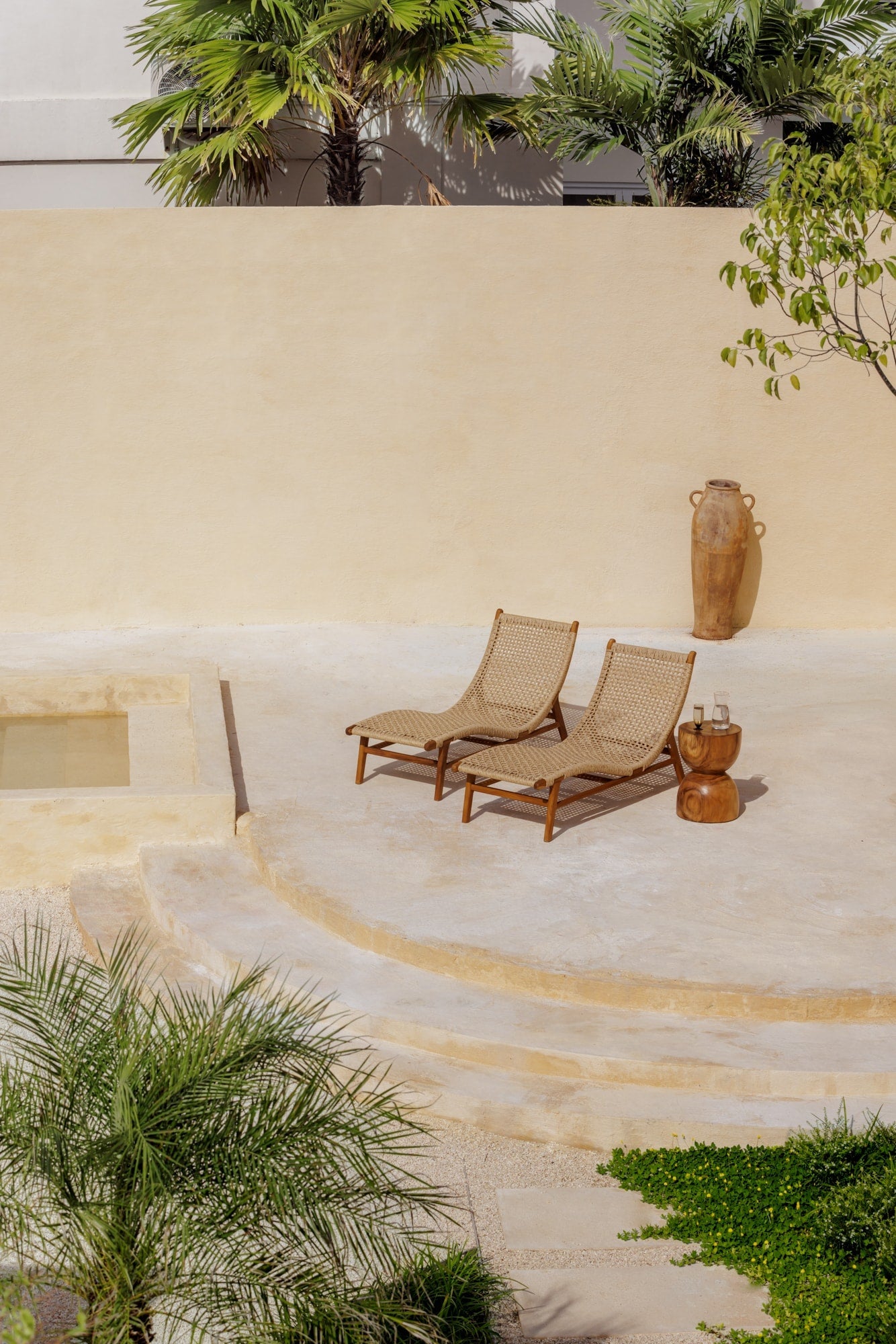 two teak and rattan lounge chairs sitting on a sun-drenched concrete deck outdoors in Bali