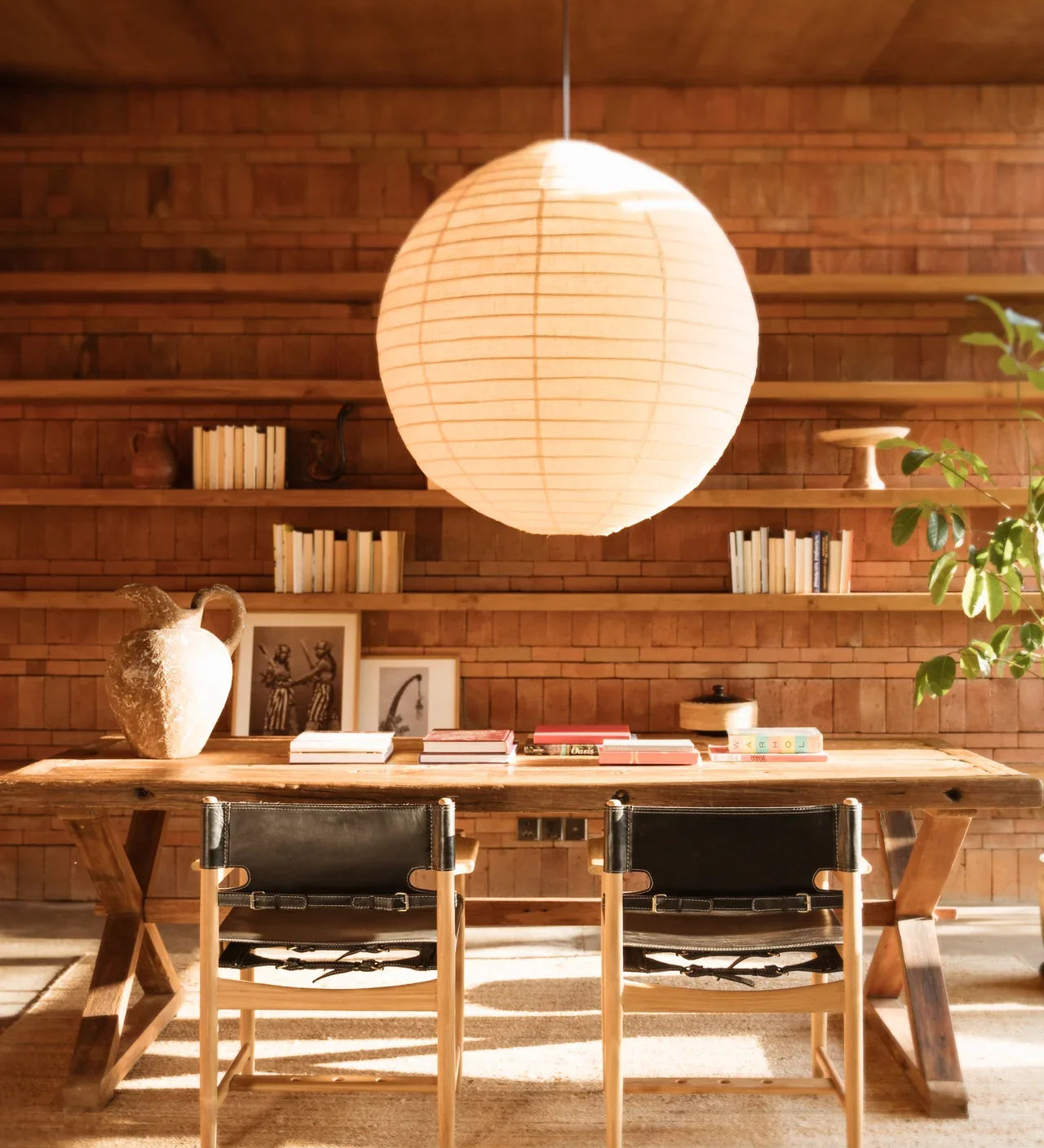 Large pendant light hanging with a teak and leather dining chair and table set