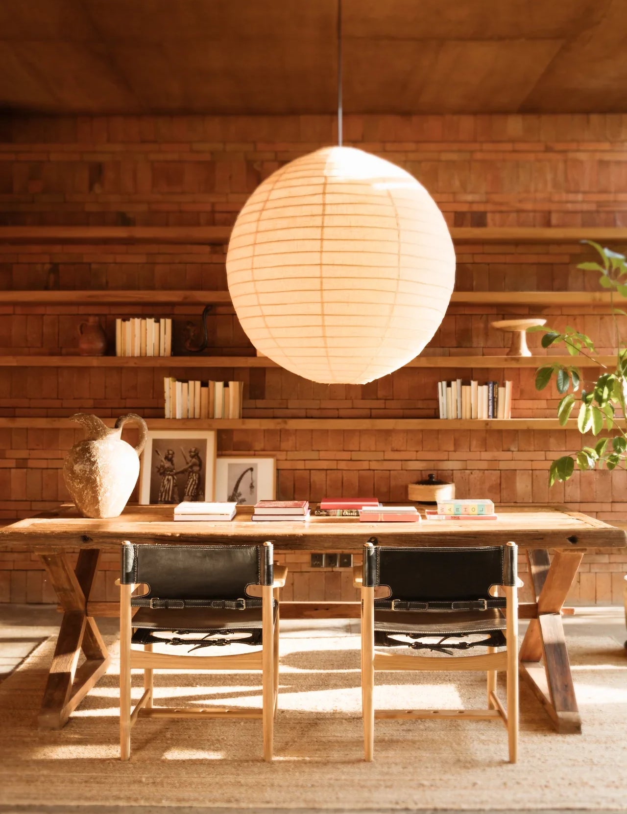 Large pendant light hanging with a teak and leather dining chair and table set