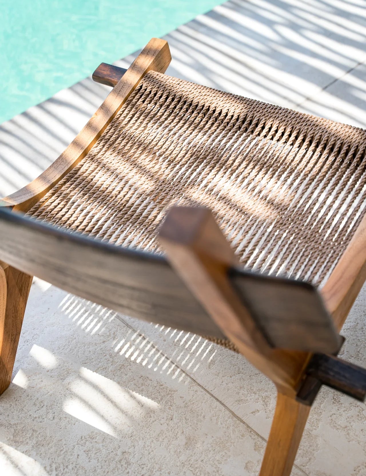 A close-up of a dark wooden and rattan lounge chair by a pool
