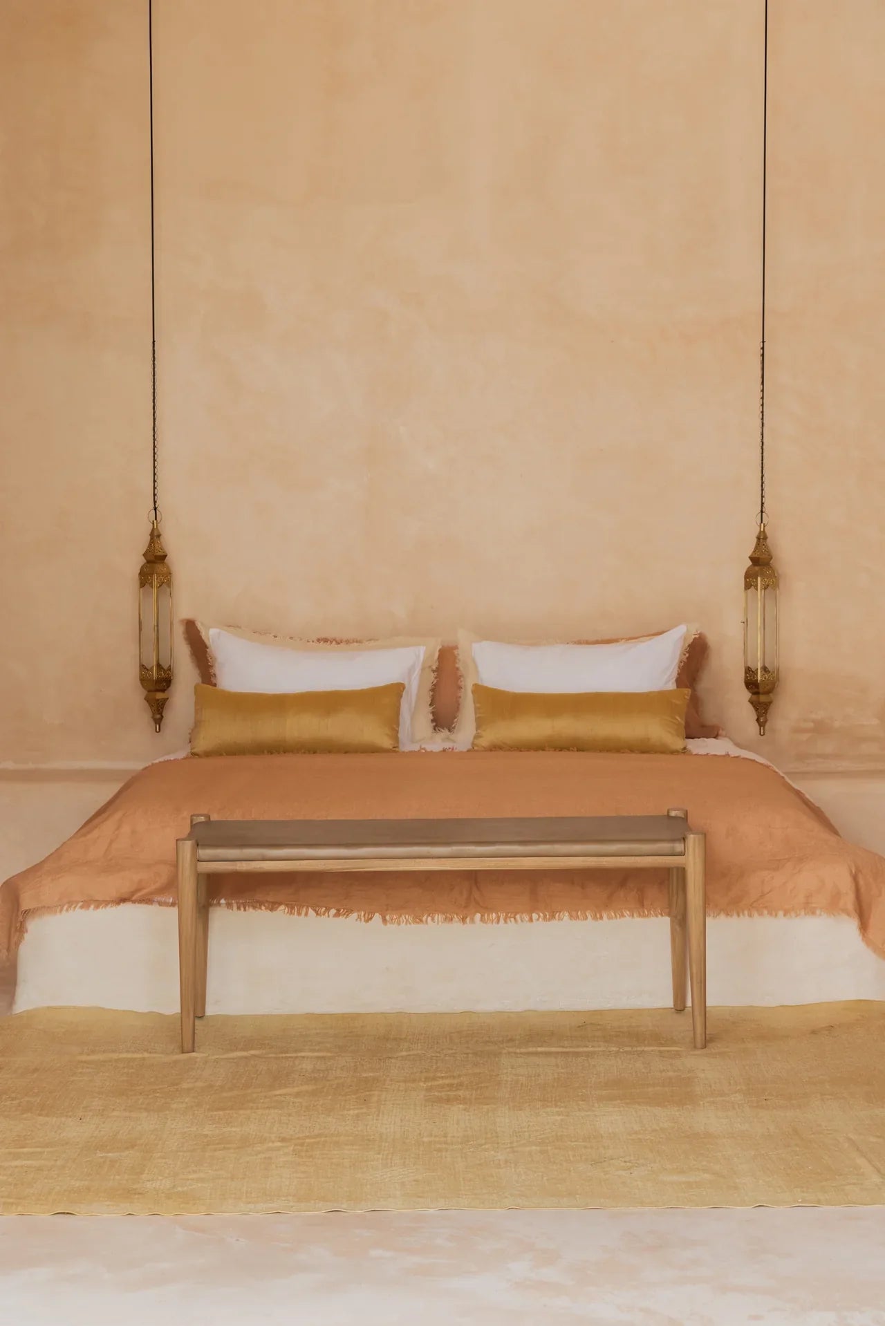 A boho bedroom with a floor bed, two hanging pendant lights and a teak and leather bench at the end of the bed. 