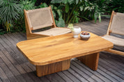 Wooden outdoor table with two chairs on a wooden deck with plants in the background