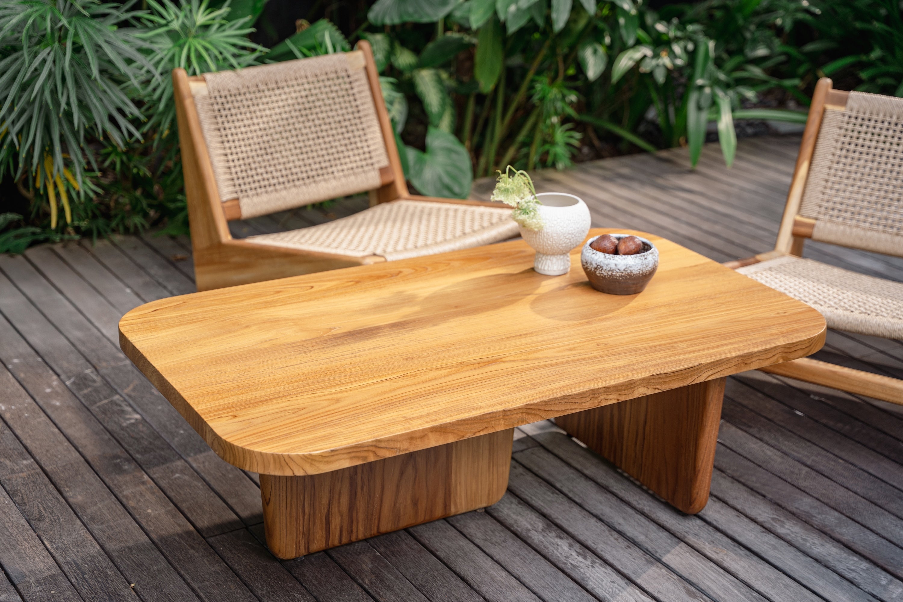 Wooden outdoor table with two chairs on a wooden deck with plants in the background